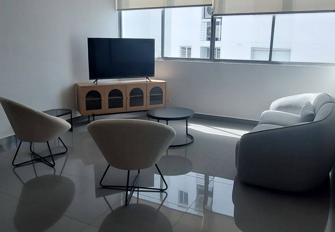 Vista general de la sala del apartamento con sus muebles, un smart tv y ventanas con vista a la ciudad